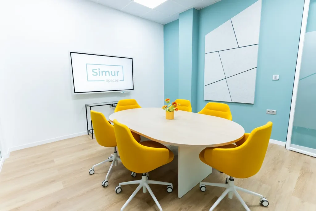 Sala de reuniones moderna en Simur Spaces Málaga con sillas amarillas y pantalla para presentaciones.