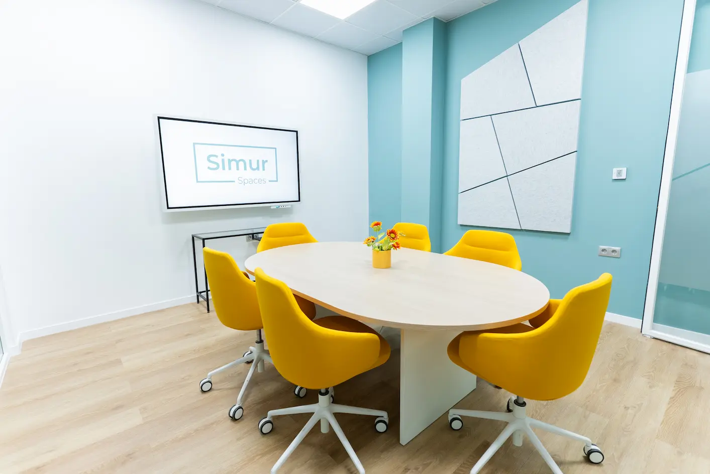 Sala de reuniones moderna en Simur Spaces Málaga con sillas amarillas y pantalla para presentaciones.